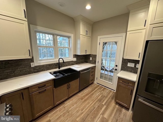 kitchen with sink, light hardwood / wood-style flooring, appliances with stainless steel finishes, white cabinetry, and decorative backsplash