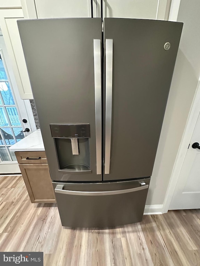 details with stainless steel refrigerator with ice dispenser, light wood-type flooring, and white cabinets