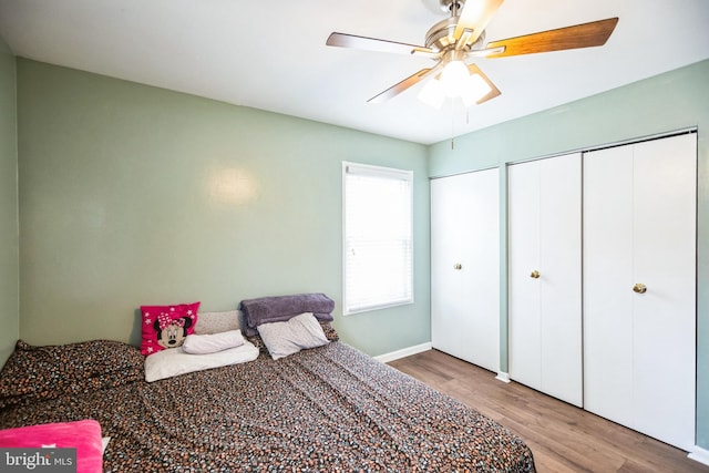 bedroom with hardwood / wood-style flooring, ceiling fan, and two closets