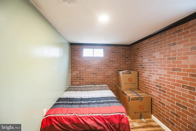 bedroom featuring brick wall and wood-type flooring