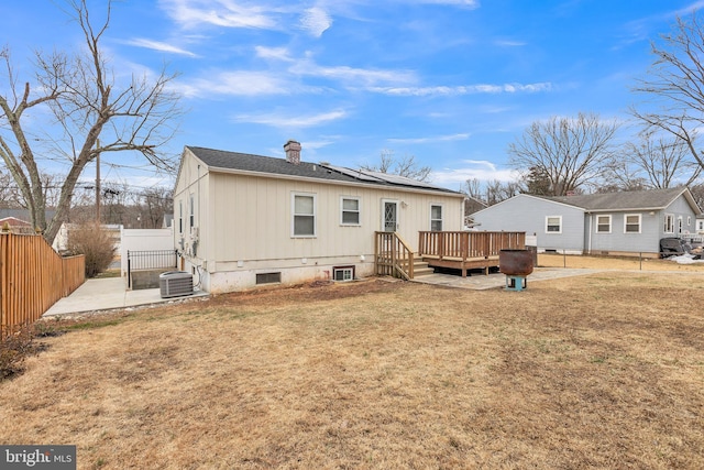 rear view of house with cooling unit, a wooden deck, a lawn, and a patio