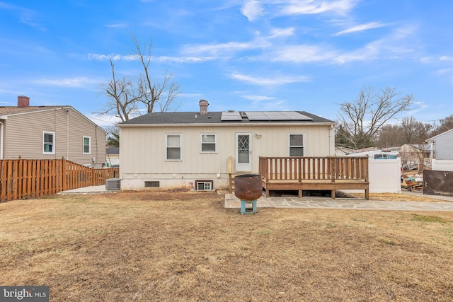 rear view of house featuring a wooden deck, cooling unit, a lawn, and solar panels