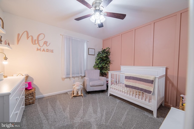 bedroom with a nursery area, ceiling fan, and dark colored carpet