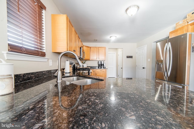 kitchen featuring appliances with stainless steel finishes, light brown cabinetry, sink, and dark stone counters