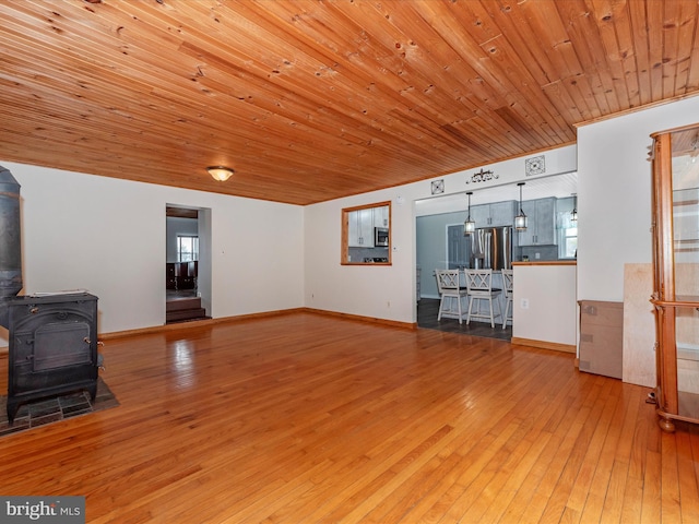 living area featuring a wood stove, wood ceiling, baseboards, and wood finished floors