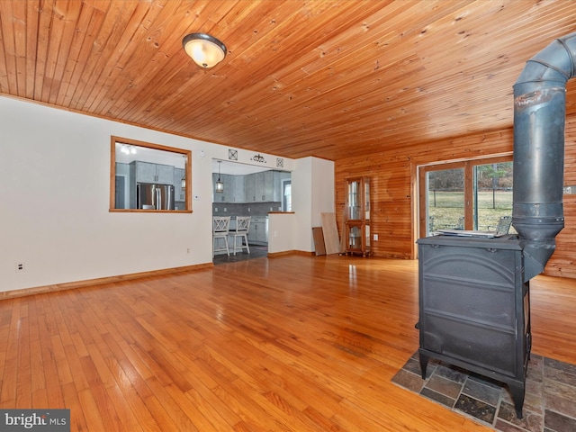 unfurnished living room with wood ceiling, wood finished floors, a wood stove, and baseboards