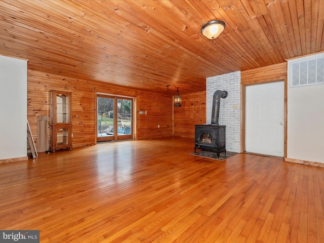 unfurnished living room featuring visible vents, wooden ceiling, a wood stove, wood walls, and light wood-style floors