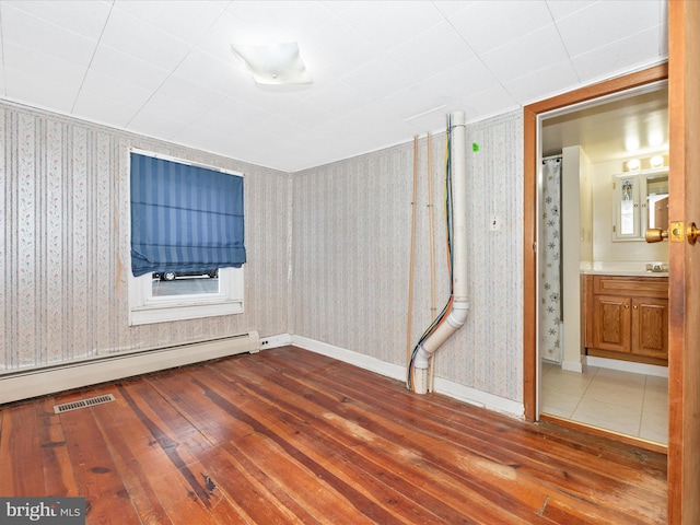 spare room featuring wallpapered walls, visible vents, baseboards, wood finished floors, and a baseboard heating unit