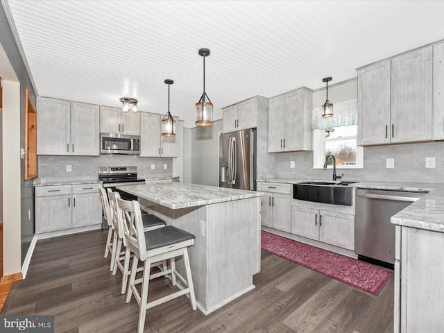 kitchen with a center island, dark wood-style flooring, decorative light fixtures, stainless steel appliances, and a sink