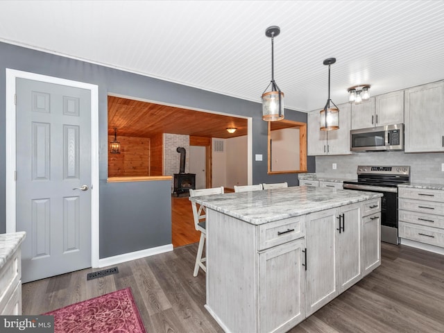 kitchen featuring dark wood-type flooring, a kitchen breakfast bar, appliances with stainless steel finishes, a center island, and pendant lighting