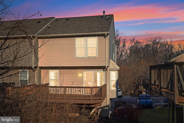 back of property at dusk with roof with shingles and a wooden deck