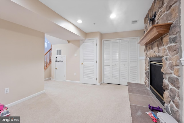 interior space featuring light carpet, baseboards, visible vents, stairway, and a fireplace