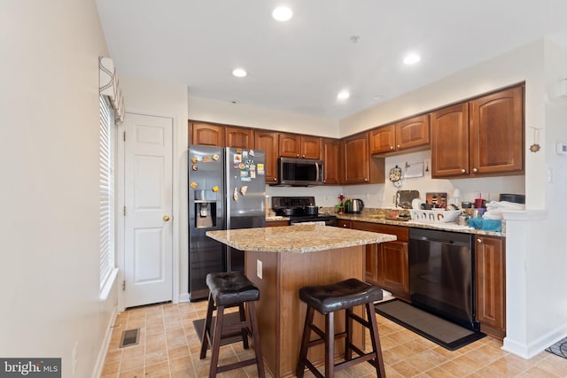 kitchen with light stone counters, a center island, visible vents, appliances with stainless steel finishes, and brown cabinetry