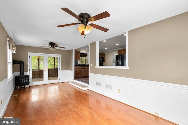 unfurnished living room featuring a ceiling fan, wood finished floors, french doors, a wainscoted wall, and visible vents