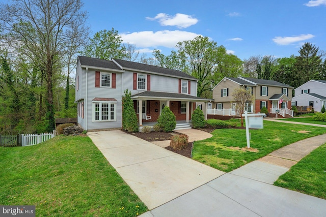 view of front facade with a front lawn, a porch, concrete driveway, and fence
