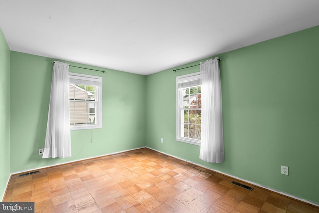 spare room featuring a wealth of natural light, visible vents, and baseboards