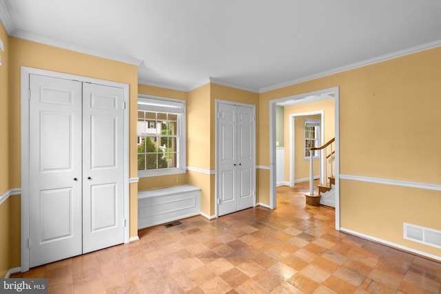 unfurnished bedroom featuring baseboards, visible vents, two closets, and crown molding