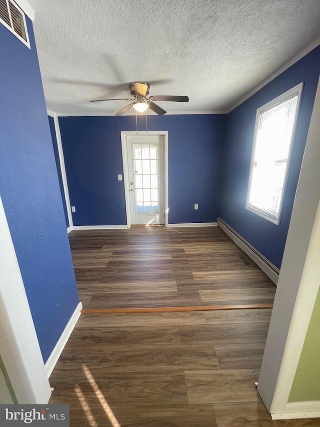 empty room with a baseboard heating unit, dark wood-type flooring, a textured ceiling, and ceiling fan