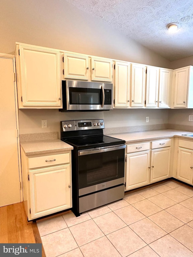 kitchen featuring stainless steel appliances, light tile patterned flooring, vaulted ceiling, and a textured ceiling