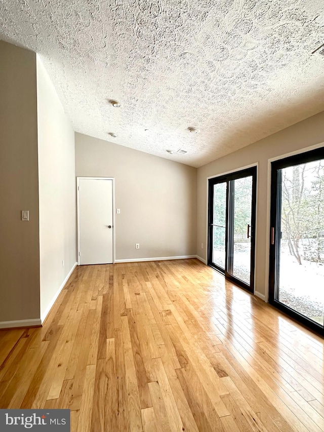 unfurnished room with lofted ceiling, a textured ceiling, and light wood-type flooring