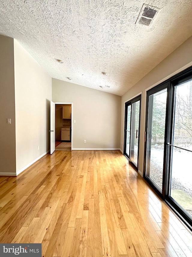 empty room with vaulted ceiling, a textured ceiling, and light wood-type flooring