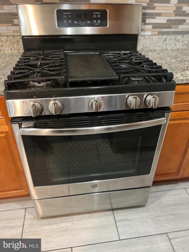 interior details with decorative backsplash, light stone countertops, and stainless steel range with gas stovetop