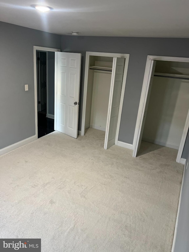 unfurnished bedroom featuring multiple closets and light colored carpet