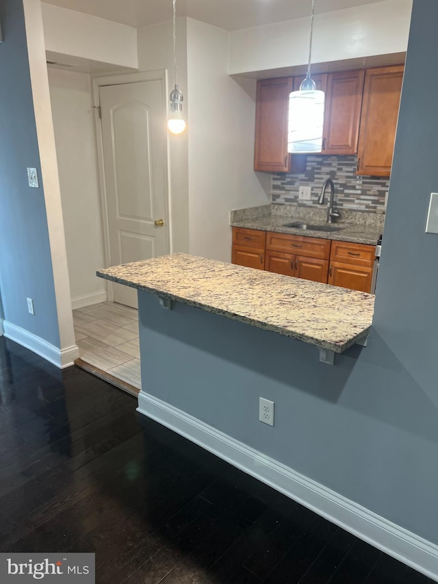 kitchen featuring a breakfast bar, pendant lighting, dark hardwood / wood-style floors, sink, and backsplash