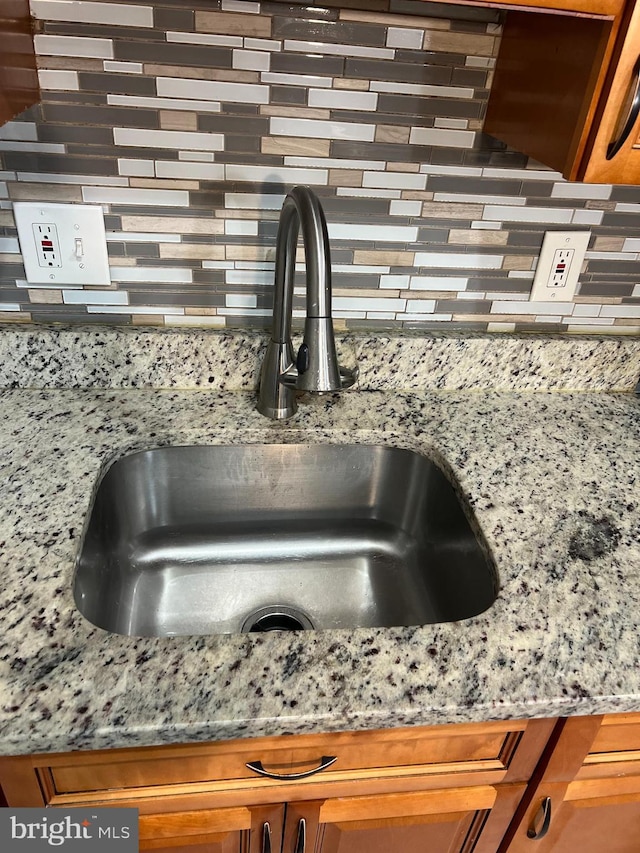 interior details with light stone countertops, sink, and backsplash