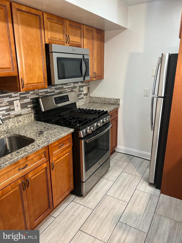 kitchen with light stone countertops, decorative backsplash, stainless steel appliances, and sink