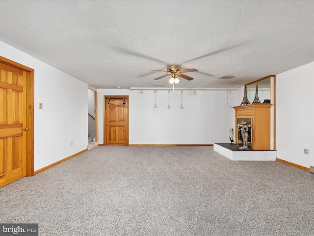 unfurnished living room featuring ceiling fan, a fireplace, a textured ceiling, and carpet flooring