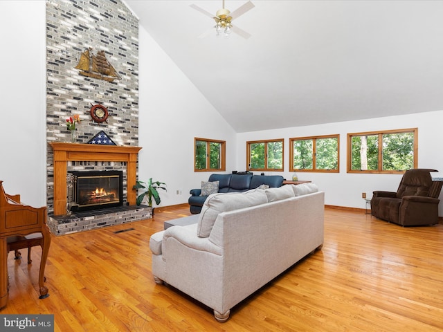 living room featuring high vaulted ceiling, a brick fireplace, and light wood-type flooring