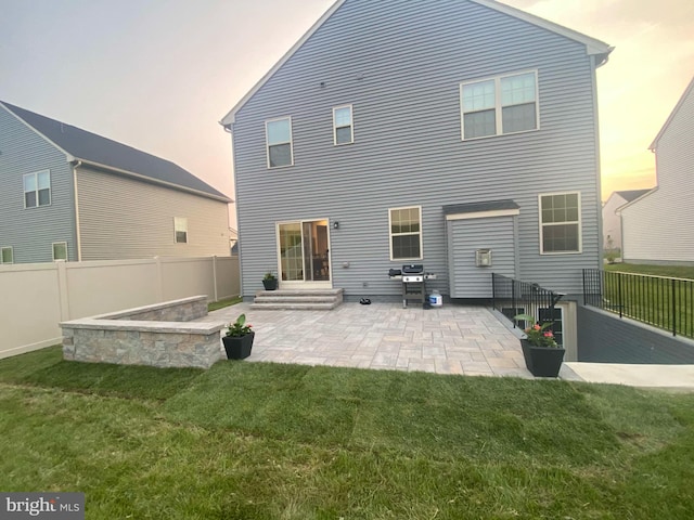 back house at dusk with a lawn and a patio area