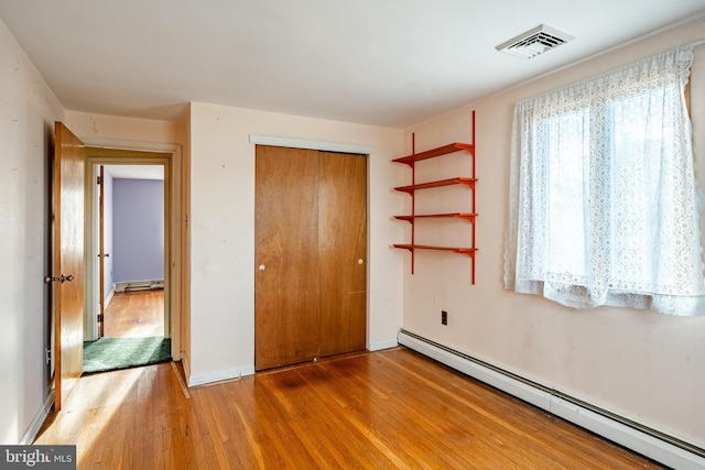 unfurnished bedroom featuring hardwood / wood-style flooring, a baseboard radiator, and a closet