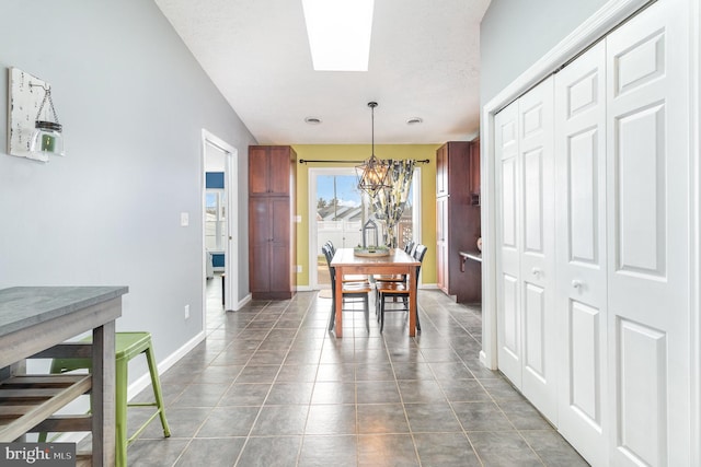 tiled dining room featuring an inviting chandelier and a skylight