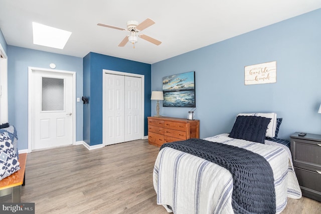 bedroom featuring ceiling fan, a skylight, a closet, and light wood-type flooring