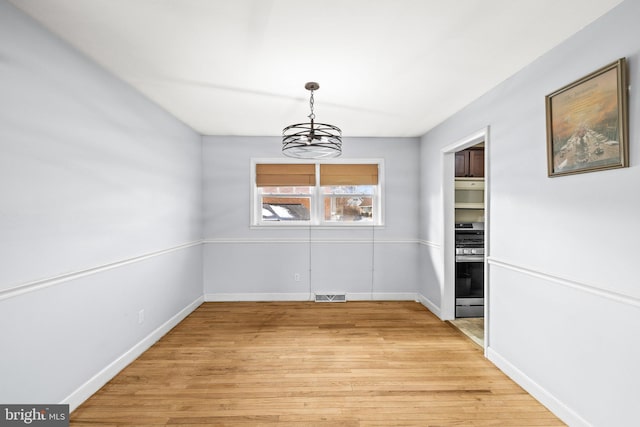 unfurnished dining area with wood-type flooring and an inviting chandelier