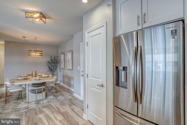 kitchen with stainless steel refrigerator with ice dispenser, light hardwood / wood-style floors, and decorative light fixtures