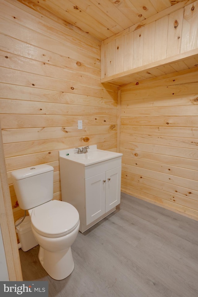 bathroom featuring hardwood / wood-style floors, wooden walls, vanity, wooden ceiling, and toilet