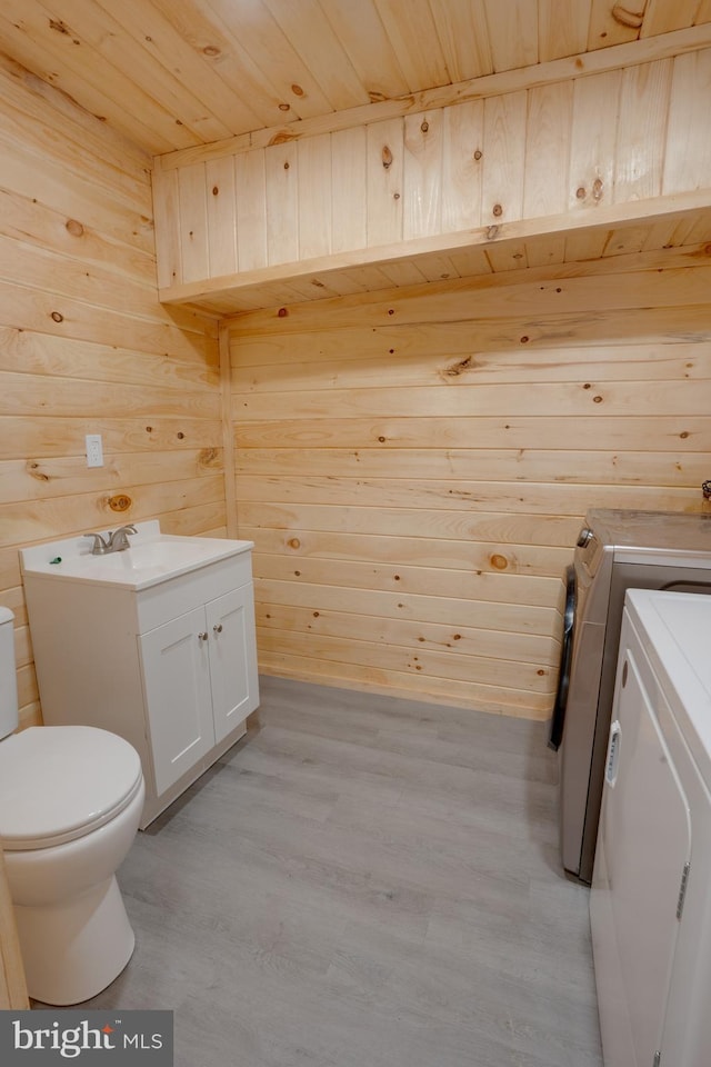 washroom with light hardwood / wood-style flooring, wood ceiling, wooden walls, and washing machine and dryer