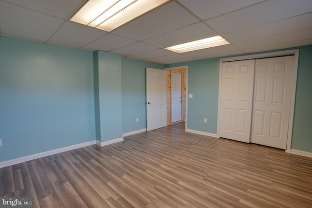 unfurnished bedroom featuring hardwood / wood-style flooring, a paneled ceiling, and a closet