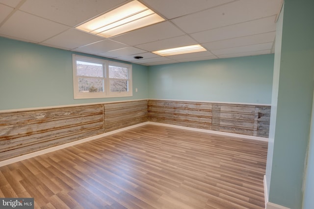 empty room featuring wood-type flooring, wooden walls, and a drop ceiling