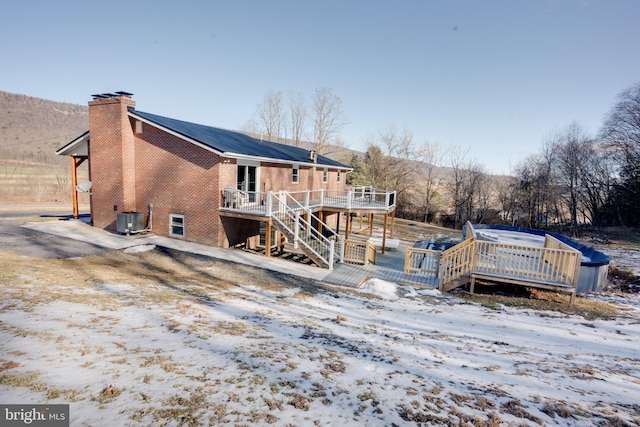 snow covered rear of property featuring central AC unit and a deck