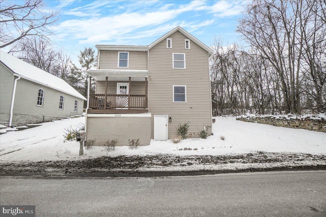 snow covered back of property featuring covered porch