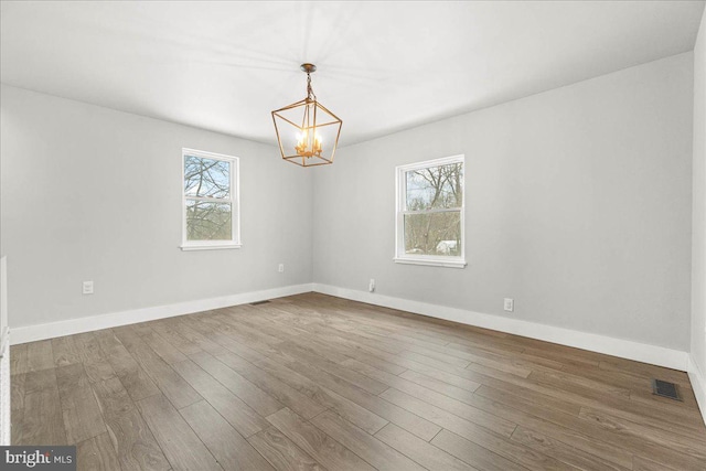 unfurnished room with an inviting chandelier, hardwood / wood-style flooring, and a wealth of natural light