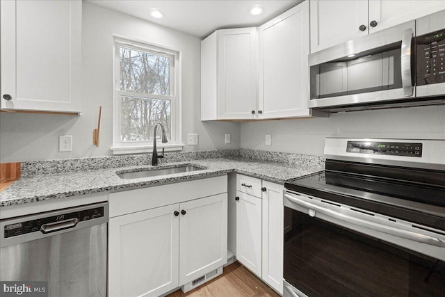 kitchen with sink, light hardwood / wood-style flooring, stainless steel appliances, light stone countertops, and white cabinets