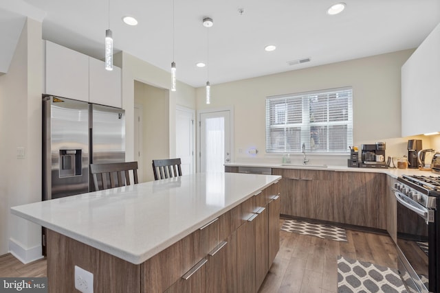 kitchen with sink, appliances with stainless steel finishes, a kitchen island, pendant lighting, and white cabinets