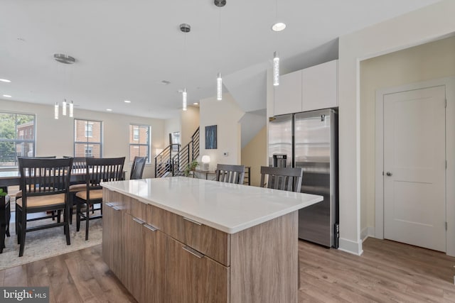 kitchen featuring a kitchen island, pendant lighting, white cabinetry, stainless steel fridge, and light hardwood / wood-style floors