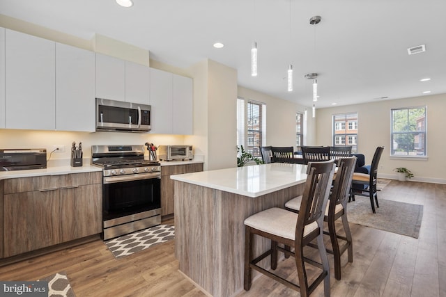 kitchen with white cabinetry, a center island, hanging light fixtures, appliances with stainless steel finishes, and light hardwood / wood-style floors