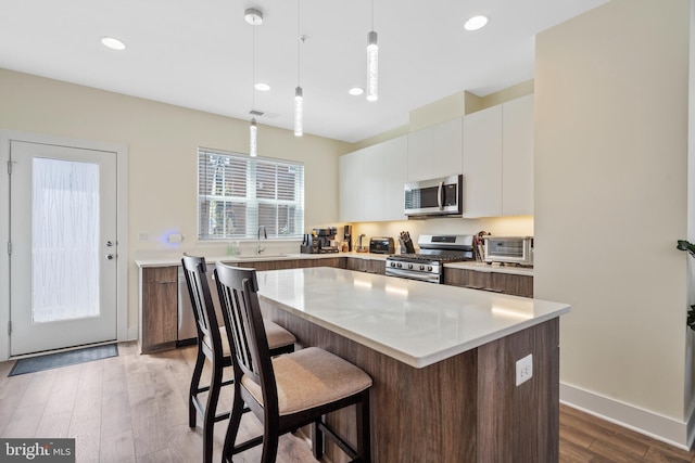 kitchen with pendant lighting, sink, white cabinetry, stainless steel appliances, and a kitchen island